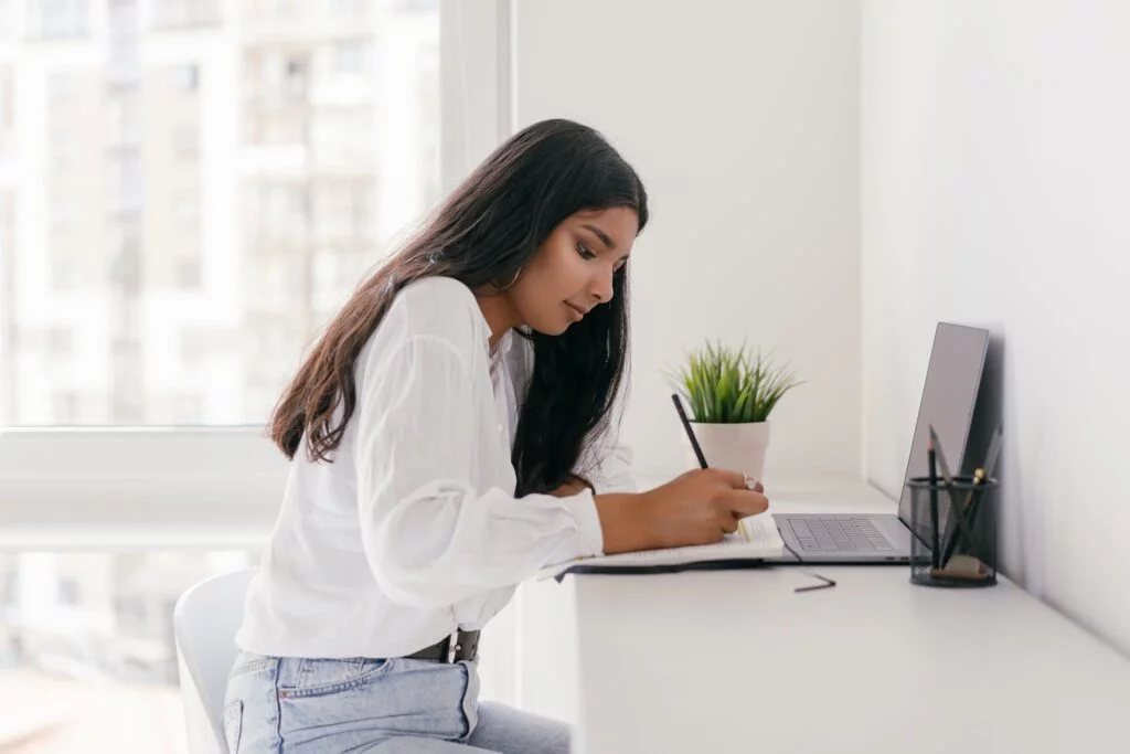 Photo by Mikhail Nilov | Chill & Thrive | Chill & Thrive A Woman Writing in the Notebook While in Front of the Laptop