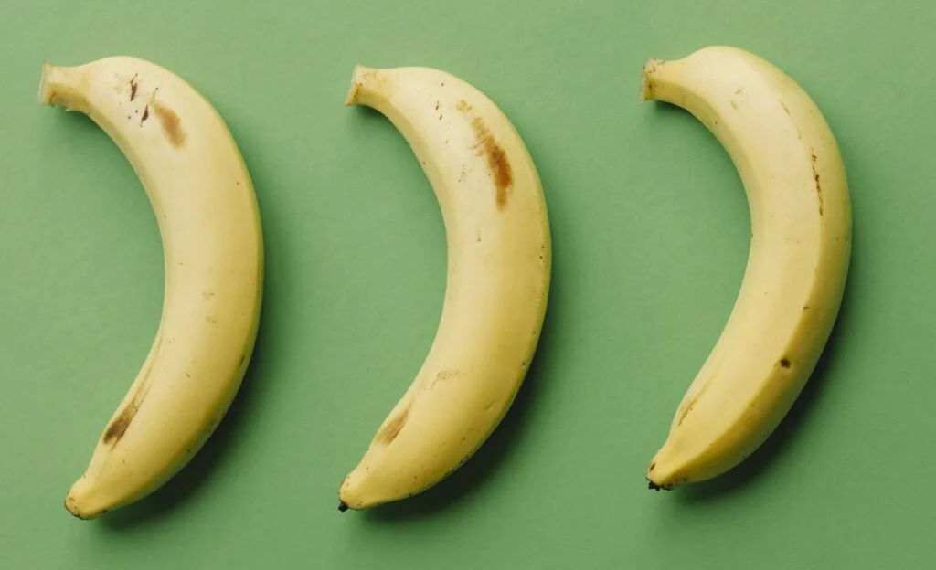 | Chill & Thrive Top view composition of healthy ripe bananas with dark spots arranged in row on green background