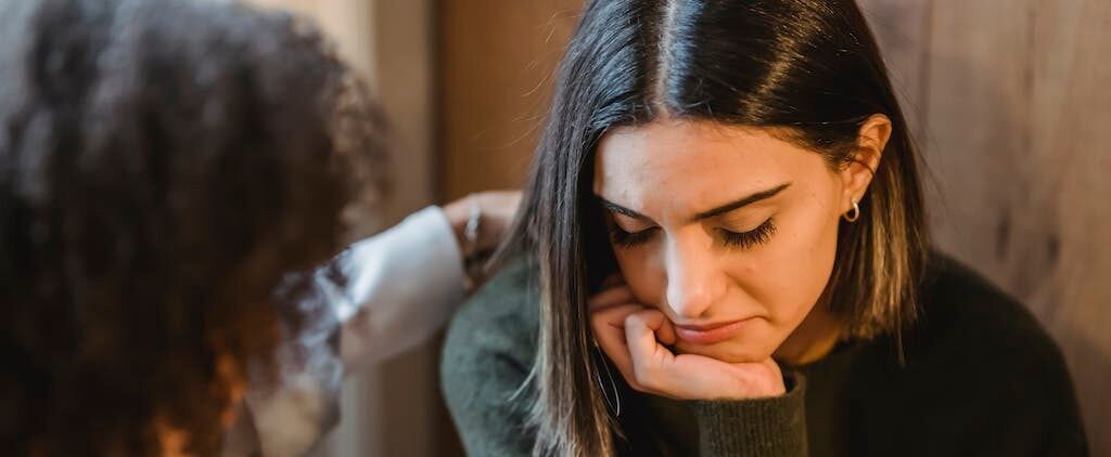 | Chill & Thrive Crop woman tapping shoulder and comforting upset female friend while sitting at home together